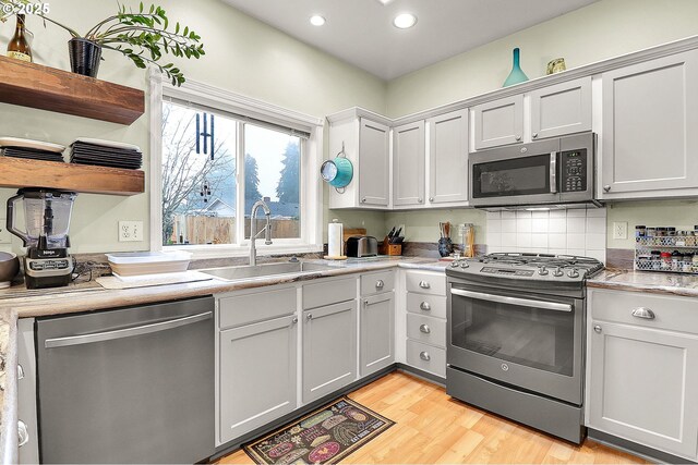 kitchen with sink, decorative backsplash, light hardwood / wood-style flooring, and stainless steel appliances