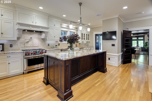 kitchen featuring luxury stove, extractor fan, ornamental molding, light wood-type flooring, and white cabinets