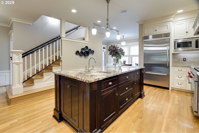 kitchen with built in appliances, a sink, ornamental molding, dark brown cabinets, and light wood-style flooring