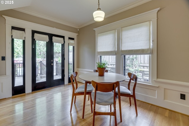 dining space featuring healthy amount of natural light, ornamental molding, light wood finished floors, a wainscoted wall, and french doors