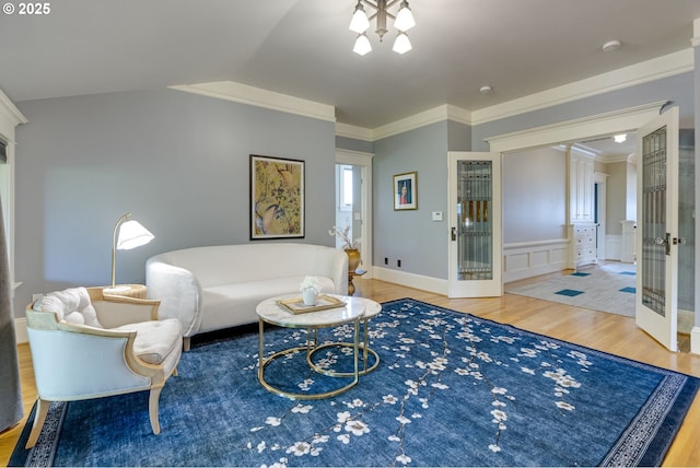 living area with wood finished floors, lofted ceiling, ornamental molding, and wainscoting