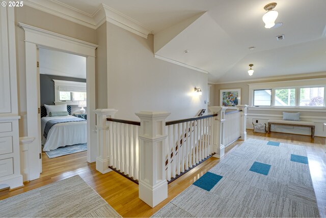 corridor with an upstairs landing, light wood-style floors, and ornamental molding