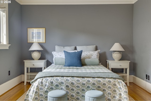 bedroom featuring wood finished floors, crown molding, and baseboards