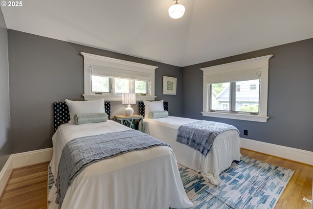bedroom with multiple windows, wood finished floors, baseboards, and vaulted ceiling