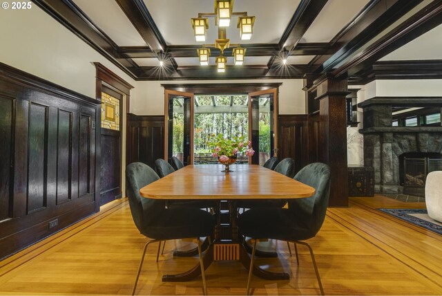 dining room featuring coffered ceiling, a fireplace, light wood finished floors, ornamental molding, and wainscoting