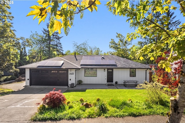 ranch-style house featuring an attached garage, a front lawn, roof mounted solar panels, and concrete driveway