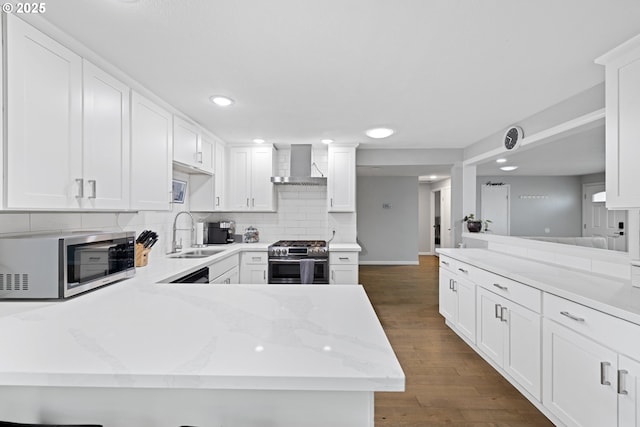 kitchen with wall chimney range hood, backsplash, a sink, a peninsula, and stainless steel appliances
