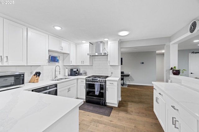 kitchen featuring decorative backsplash, appliances with stainless steel finishes, a sink, white cabinets, and wall chimney exhaust hood
