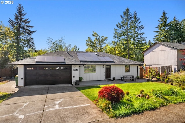 ranch-style home with a front lawn, fence, an attached garage, driveway, and solar panels
