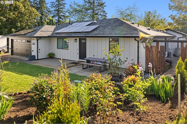 view of front of property featuring an attached garage, solar panels, roof with shingles, and a front lawn