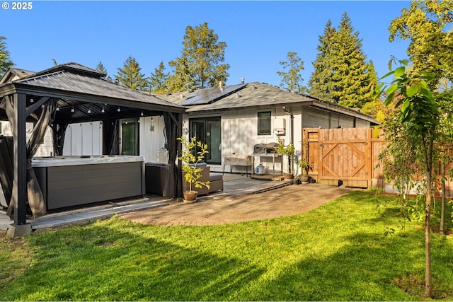 rear view of property with a hot tub, a lawn, a gazebo, and solar panels