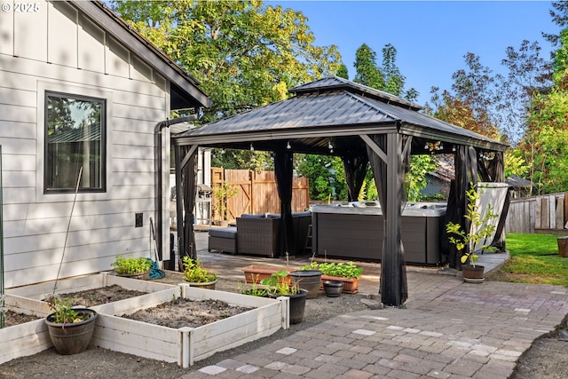 view of patio featuring an outdoor living space, a vegetable garden, a hot tub, a gazebo, and fence