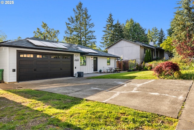 view of front of property with board and batten siding, driveway, solar panels, a garage, and a front lawn