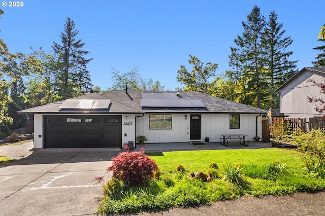 ranch-style house featuring a front lawn, roof mounted solar panels, board and batten siding, concrete driveway, and an attached garage
