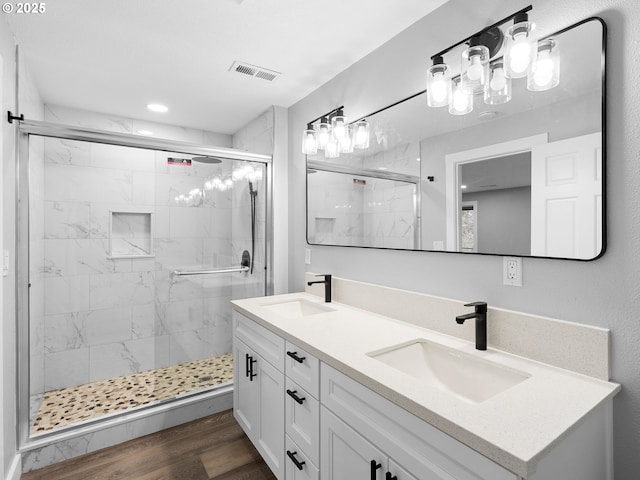 full bath featuring a marble finish shower, visible vents, a sink, and wood finished floors