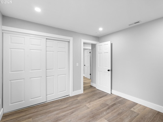 unfurnished bedroom with recessed lighting, wood finished floors, visible vents, baseboards, and a closet