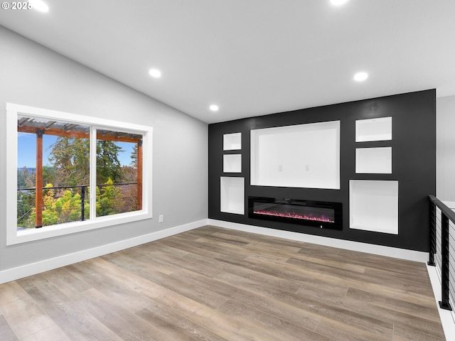 unfurnished room featuring lofted ceiling, recessed lighting, baseboards, light wood finished floors, and a glass covered fireplace