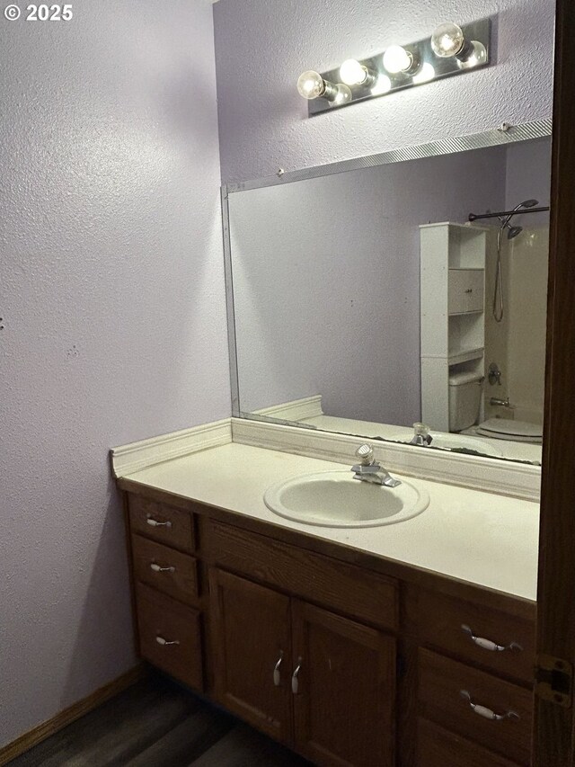 bathroom with vanity, a textured wall, toilet, wood finished floors, and a shower