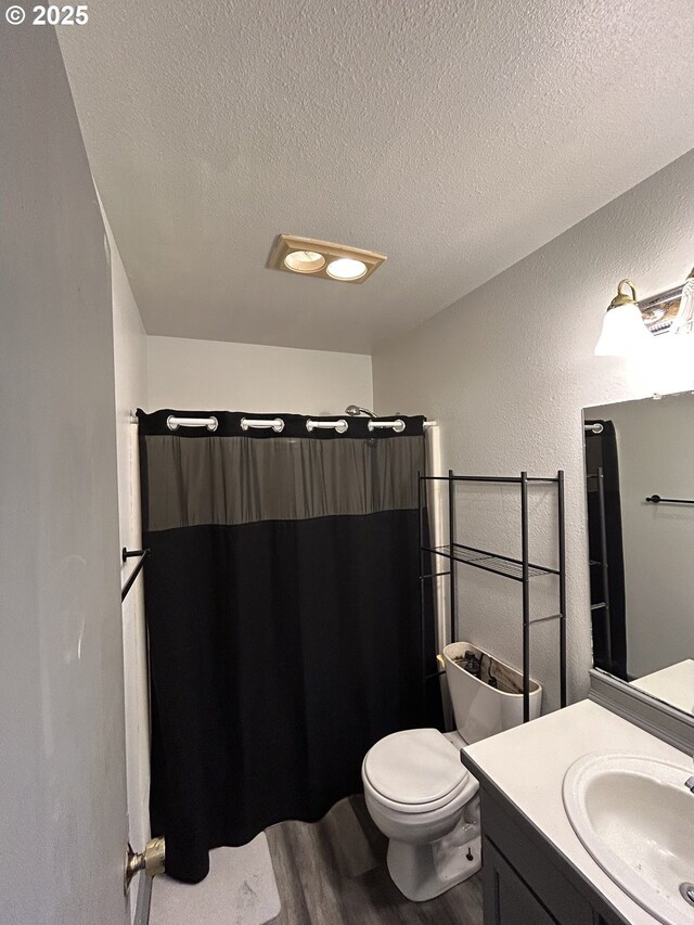 bathroom with a textured ceiling, vanity, wood finished floors, toilet, and curtained shower