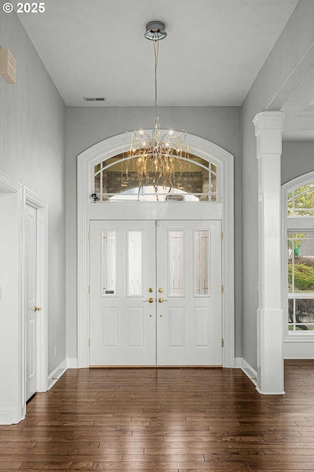 foyer entrance featuring a chandelier, baseboards, vaulted ceiling, wood-type flooring, and ornate columns