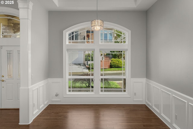 foyer featuring dark wood-style floors, a wainscoted wall, decorative columns, and a notable chandelier