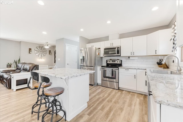 kitchen with backsplash, stainless steel appliances, sink, white cabinets, and a kitchen island