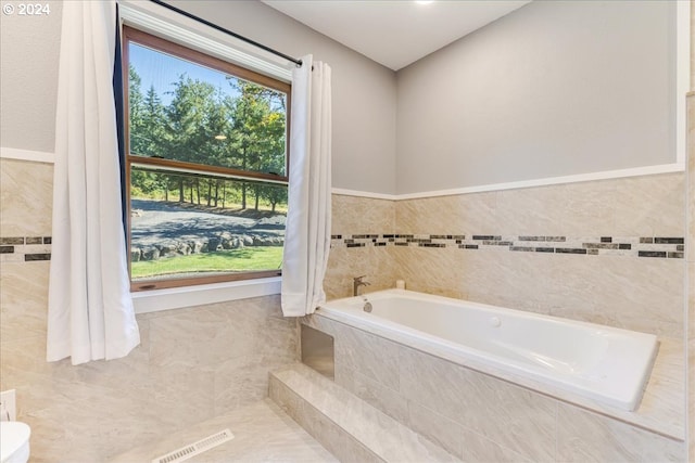 bathroom featuring a relaxing tiled tub and tile walls