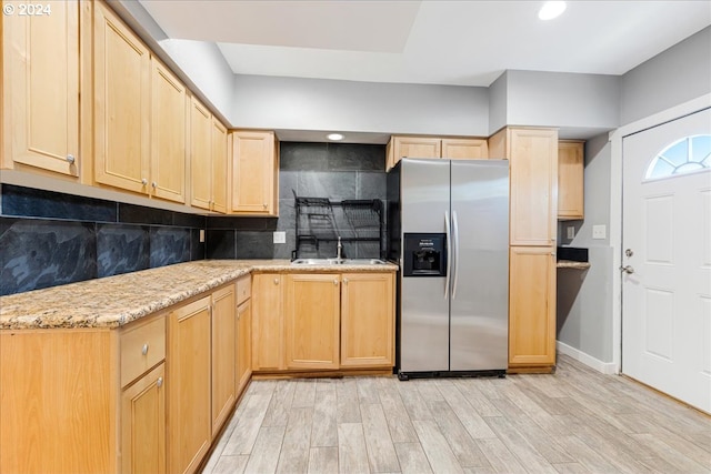 kitchen with stainless steel refrigerator with ice dispenser, decorative backsplash, light stone countertops, light brown cabinetry, and light hardwood / wood-style floors