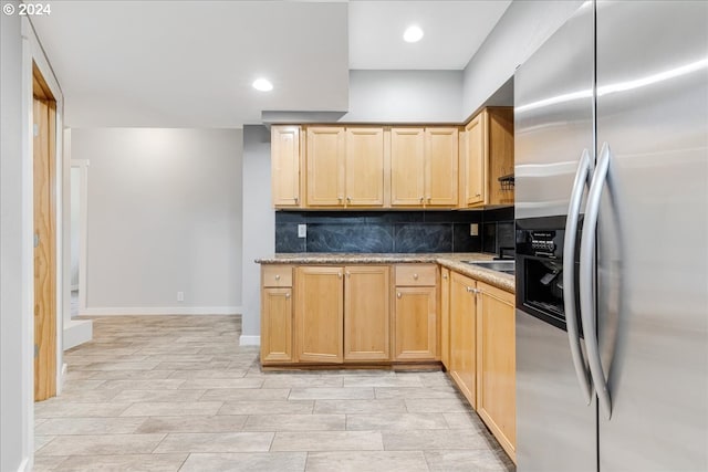 kitchen featuring light brown cabinets, light stone counters, light hardwood / wood-style flooring, stainless steel refrigerator with ice dispenser, and backsplash