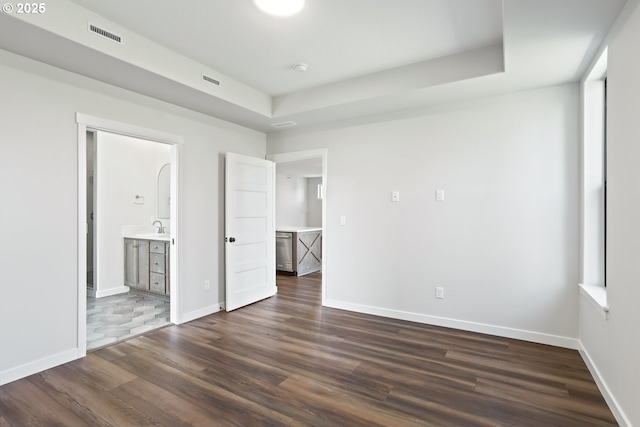 unfurnished bedroom with dark wood-style floors, baseboards, ensuite bathroom, and visible vents