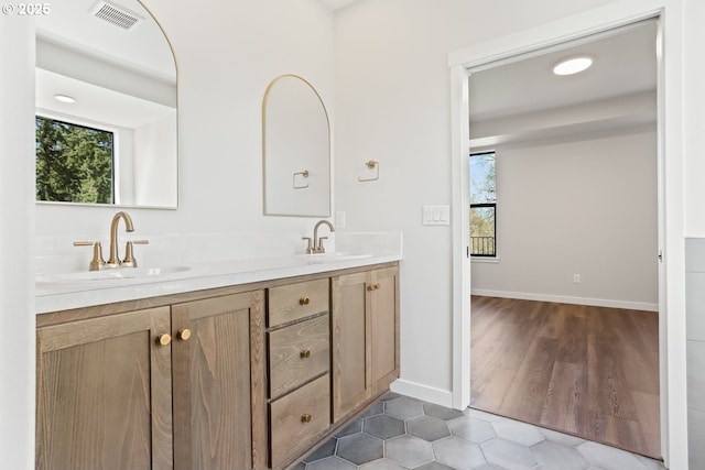 full bathroom featuring baseboards, a sink, visible vents, and double vanity