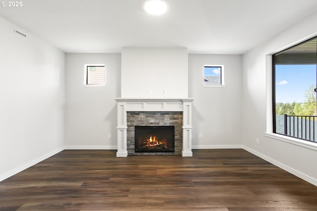 unfurnished living room with a warm lit fireplace, baseboards, visible vents, and dark wood-style floors