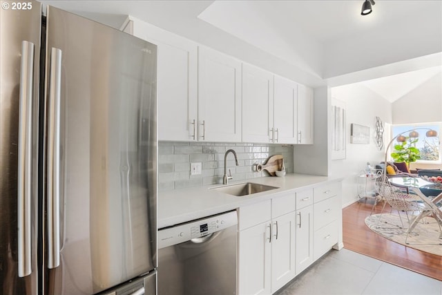 kitchen with vaulted ceiling, a sink, stainless steel appliances, light countertops, and white cabinetry