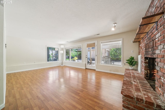 17476 SW Edy Rd, Sherwood, OR 97140 - unfurnished living room featuring a brick fireplace, wood finished floors, a textured ceiling, and baseboards