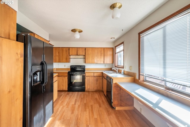 kitchen featuring black appliances, light countertops, light wood-style flooring, a textured ceiling, and a sink