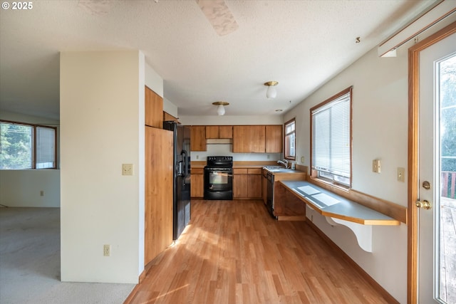 kitchen with a sink, black appliances, light countertops, under cabinet range hood, and brown cabinets