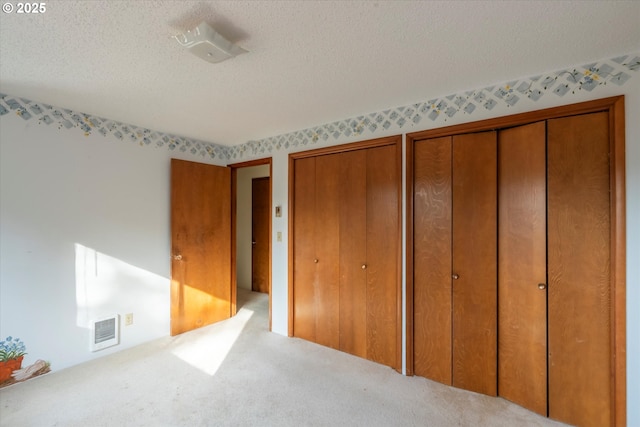 unfurnished bedroom featuring visible vents, two closets, a textured ceiling, and carpet