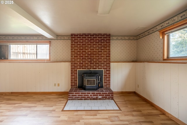 unfurnished living room with wood finished floors, a wood stove, a healthy amount of sunlight, and beamed ceiling