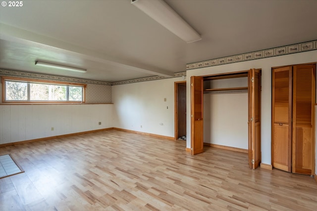 unfurnished bedroom with light wood-style flooring, baseboards, and multiple closets