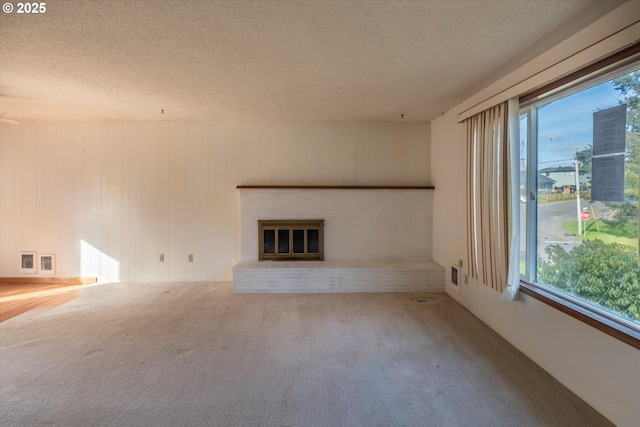 unfurnished living room with carpet flooring, a fireplace, a wealth of natural light, and a textured ceiling