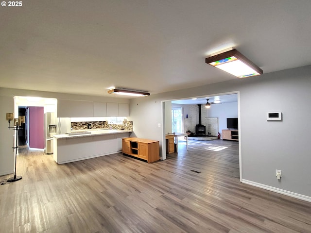 kitchen with tasteful backsplash, stainless steel fridge with ice dispenser, a wood stove, kitchen peninsula, and light hardwood / wood-style floors