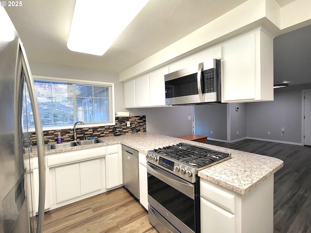 kitchen with stainless steel appliances, white cabinetry, sink, and light hardwood / wood-style floors