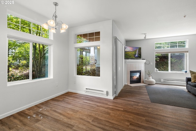 unfurnished living room featuring a baseboard heating unit, a chandelier, a tile fireplace, and wood finished floors