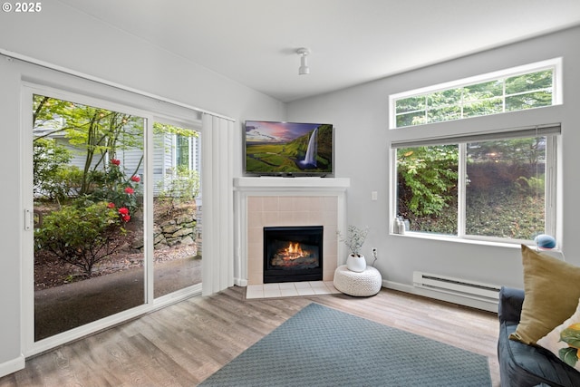 sitting room with baseboard heating, a tile fireplace, wood finished floors, and plenty of natural light