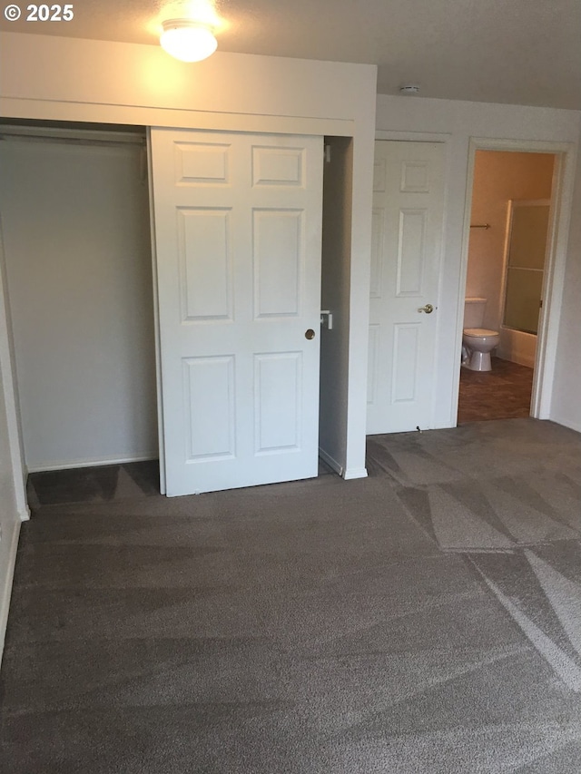 unfurnished bedroom featuring ensuite bath, a closet, and dark colored carpet