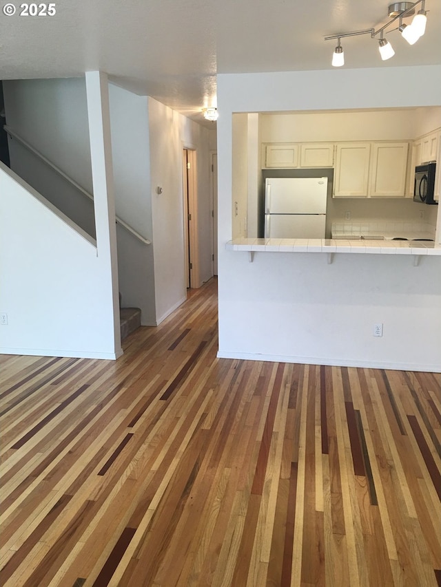 kitchen featuring white cabinetry, hardwood / wood-style flooring, kitchen peninsula, and white refrigerator