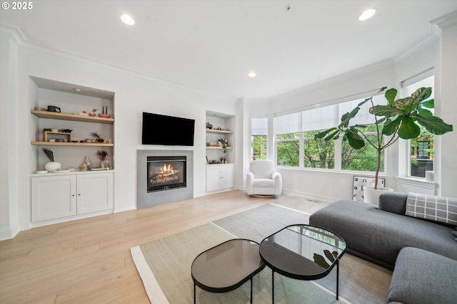 living area with a glass covered fireplace, ornamental molding, built in features, and light wood-style floors