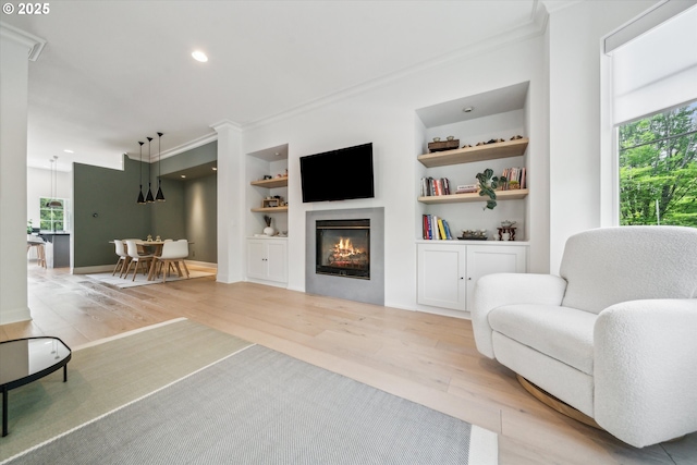 living area with crown molding, built in features, and light wood finished floors