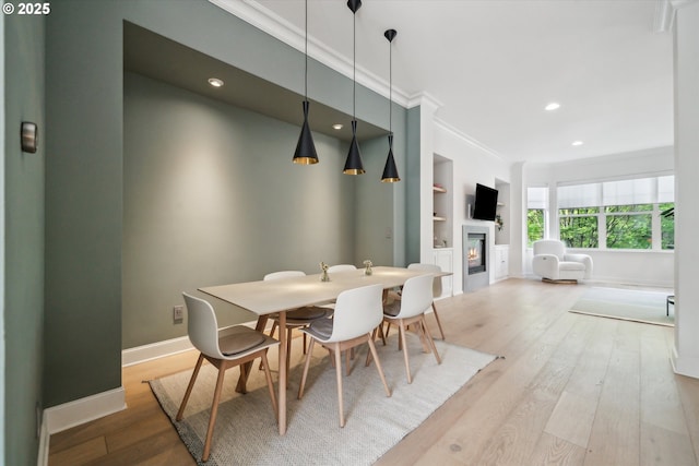 dining area featuring baseboards, ornamental molding, a glass covered fireplace, and wood finished floors