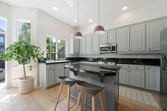 kitchen featuring dark countertops, a breakfast bar area, stainless steel microwave, a sink, and light wood finished floors